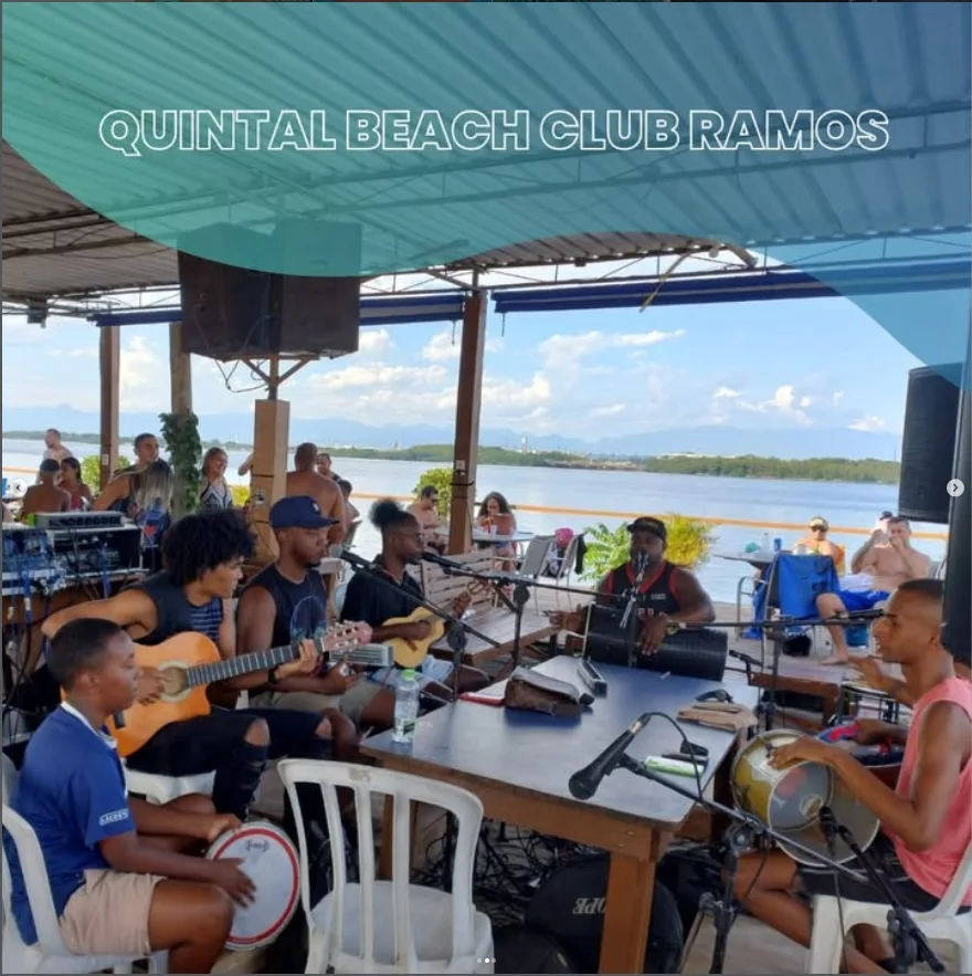 Roda de pagode com músicos reunidos à mesa no Quintal, junto à água